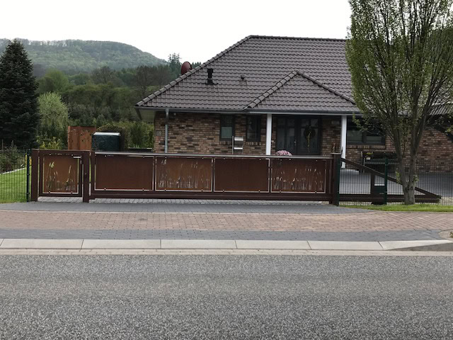 Modernes Schiebetor aus Cortenstahl in Rost-Optik mit integrierter Pforte und vertikaler Musterung vor einem Wohnhaus, von Tore & Torsysteme von Stahl- und Metallbau Drost.