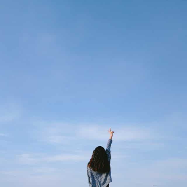 Girl in denim points her finger towards a blue sky