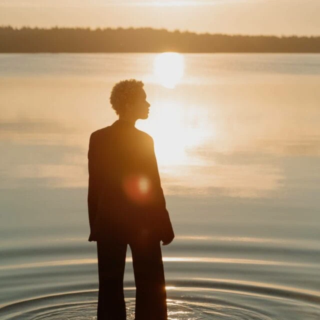 Stages of Grief: A girl stands in water staring out at the sunset