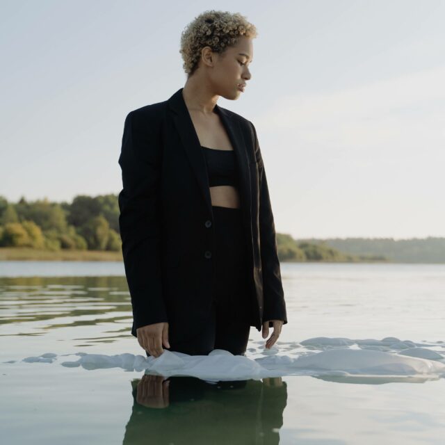 Stages Of Grief: Anger. A girl stares out while half submerged in water, fully clothed