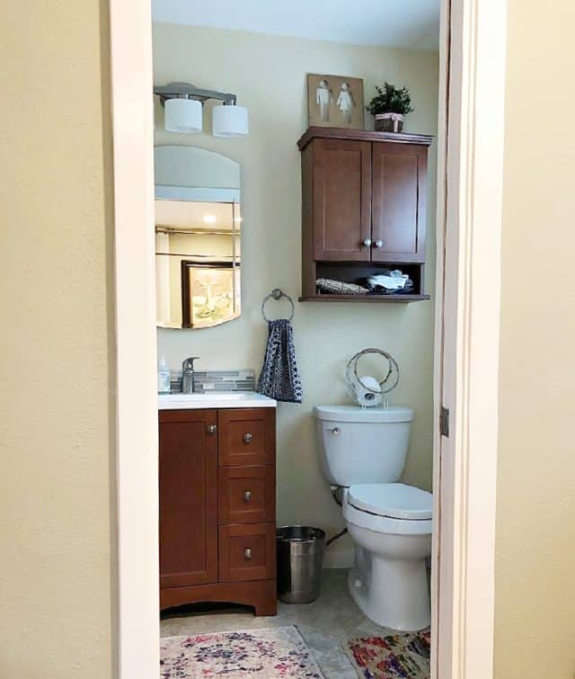 Bathroom Before with light yellows brown cabinet and sink and brown over the toilet cabinet
