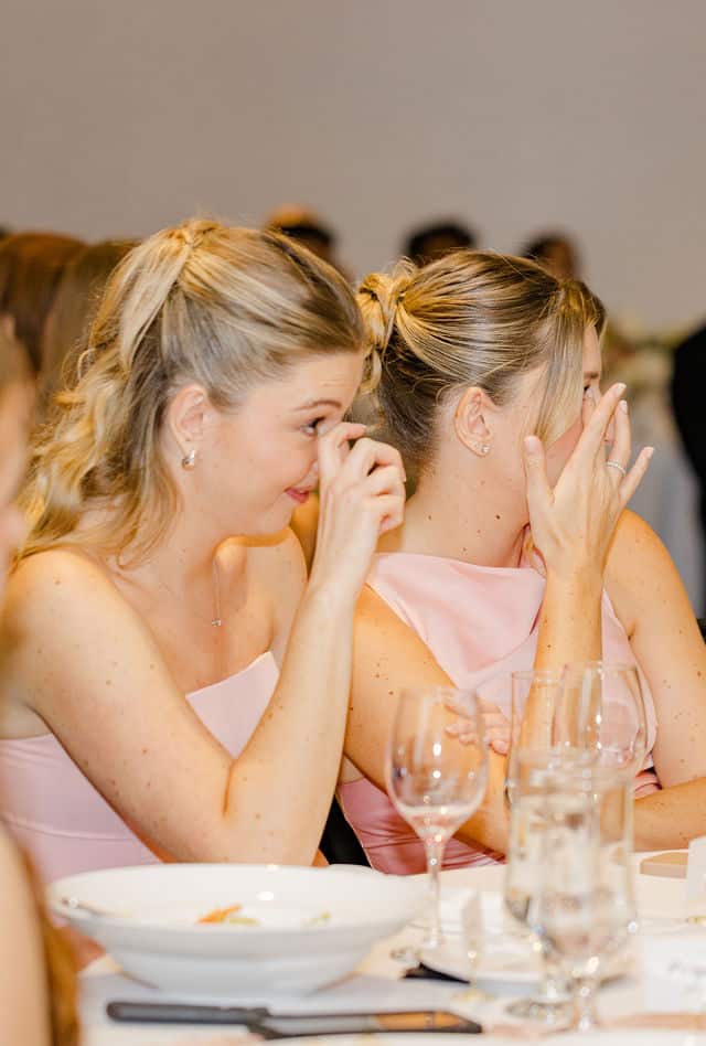 Two bridesmaids wiping away happy tears during the wedding speeches