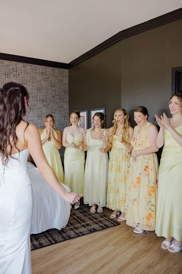 Bride revealing her wedding gown to her bridesmaids in yellow dresses at Brookstreet Hotel
