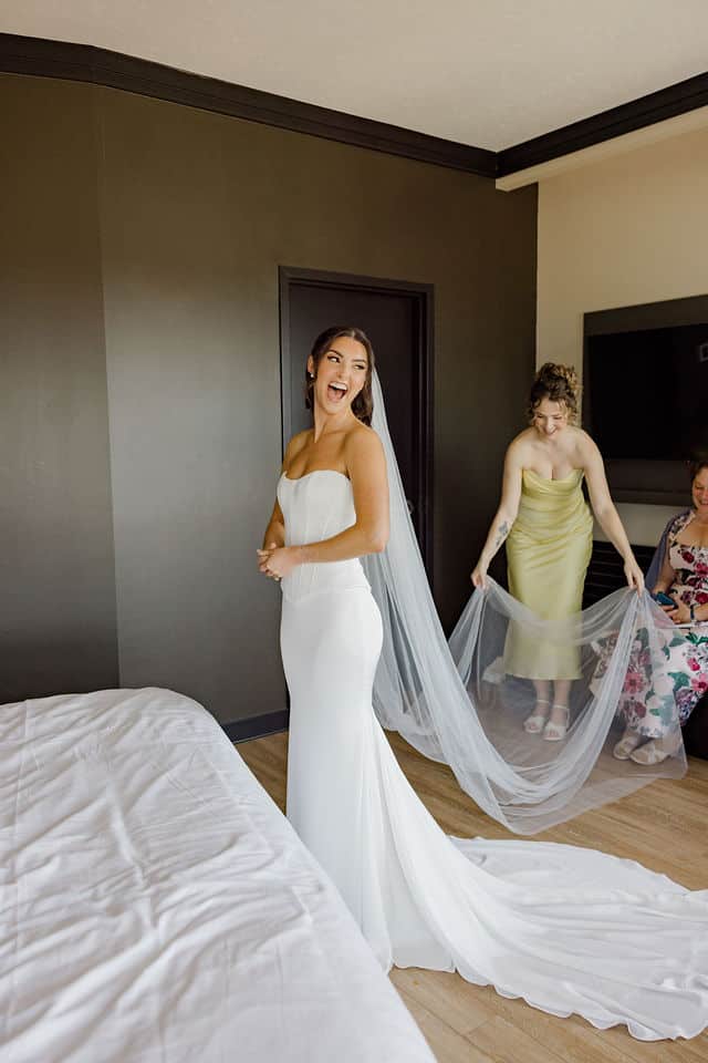 Bride laughing as a bridesmaid arranges her veil in her wedding gown at Brookstreet Hotel