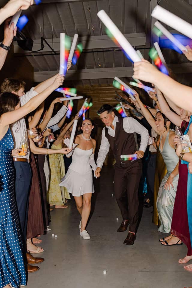Julia and Will walking hand in hand through the guests' glow stick tunnel during her outfit change reveal