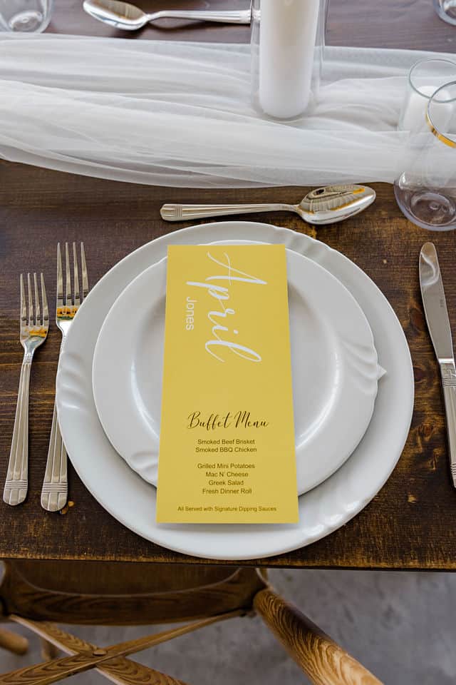Wedding reception place setting with a yellow buffet menu card listing the Meatings barbecue dinner