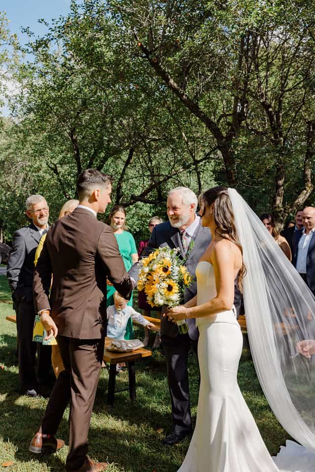 Groom shaking hands with the bride's father as she arrives for the ceremony under the apple trees