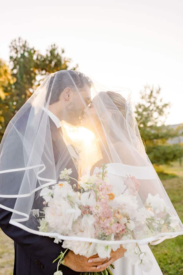 Bride and groom sharing a kiss under the veil at golden hour