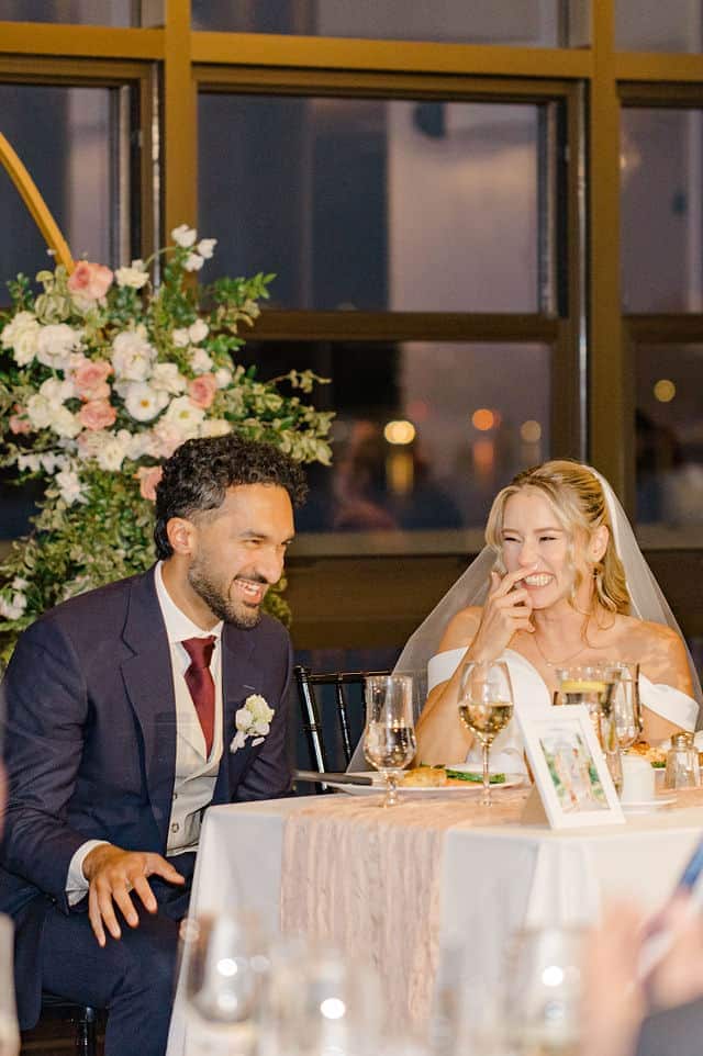 Bride and groom laughing together at the sweetheart table during reception speeches