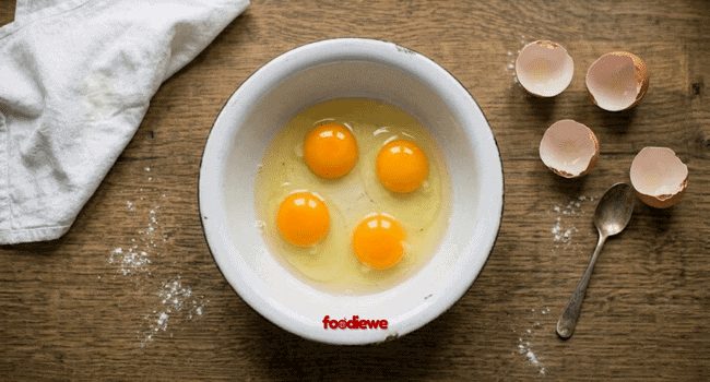 Four eggs cracked open in a steel bowl for egg paratha filling
