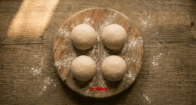 Four equal dough balls on a wooden chakla for rolling egg parathas