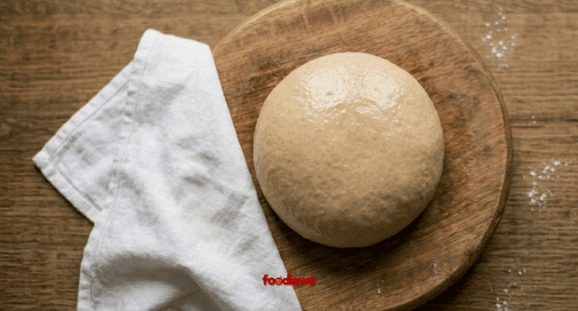 Smooth soft wheat dough ball resting on a wooden chakla covered with a damp cloth
