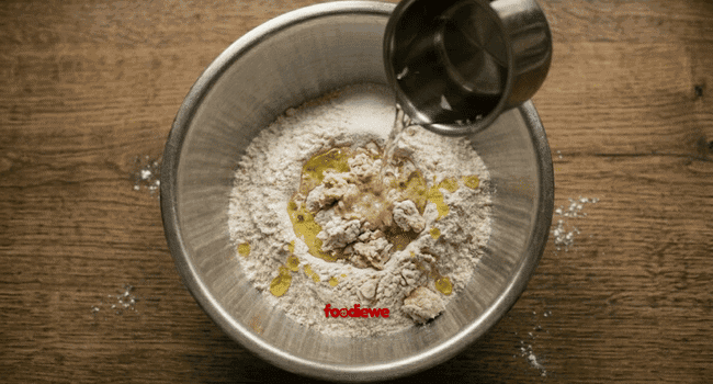 Water being poured into wheat flour to make egg paratha dough