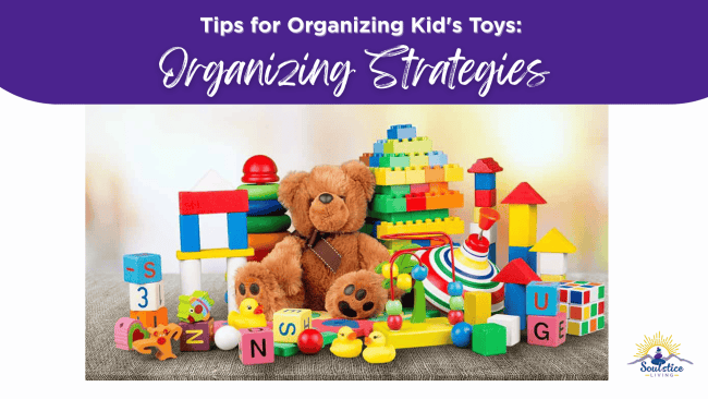 Colorful children's toys including a teddy bear, building blocks, rubber ducks, and stacking rings arranged on a grey surface for organizing kids' toys.