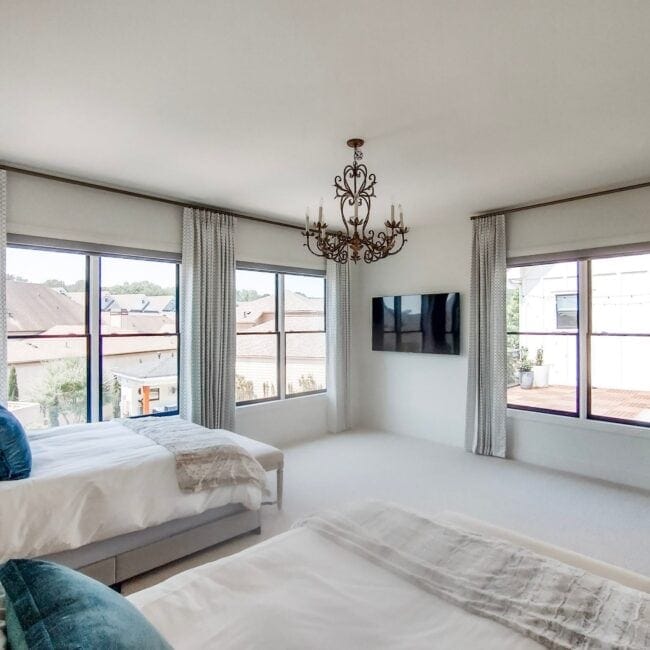 Spacious bedroom with large windows, contemporary decor, and a ceiling chandelier for natural elegance.