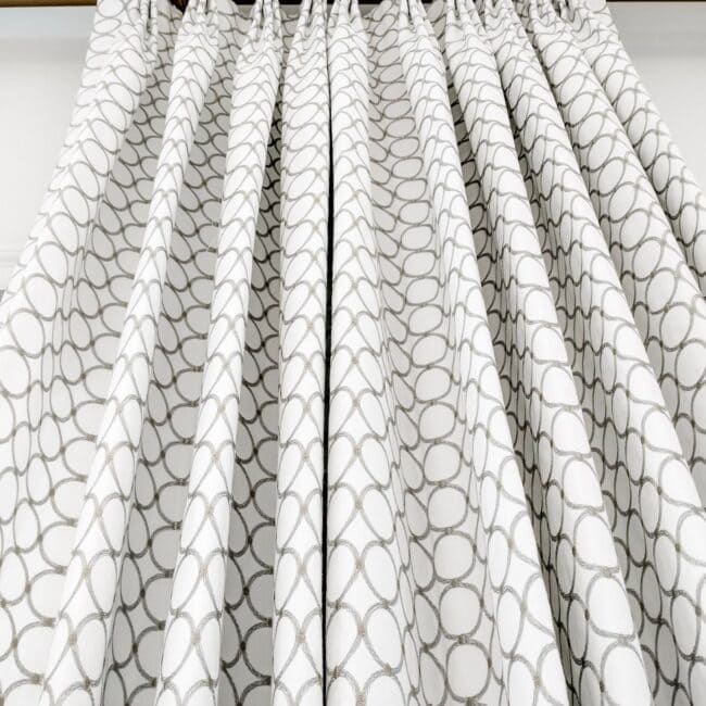Stylish white curtains with grey circular design hanging in a room.