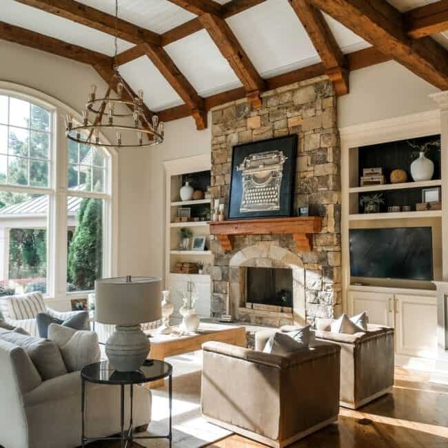 Elegant living room with stone fireplace, large windows, cozy seating, and decorative shelves.