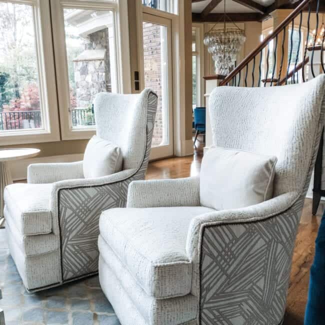 Elegant white upholstered armchairs with decorative fabric patterns and pillows.