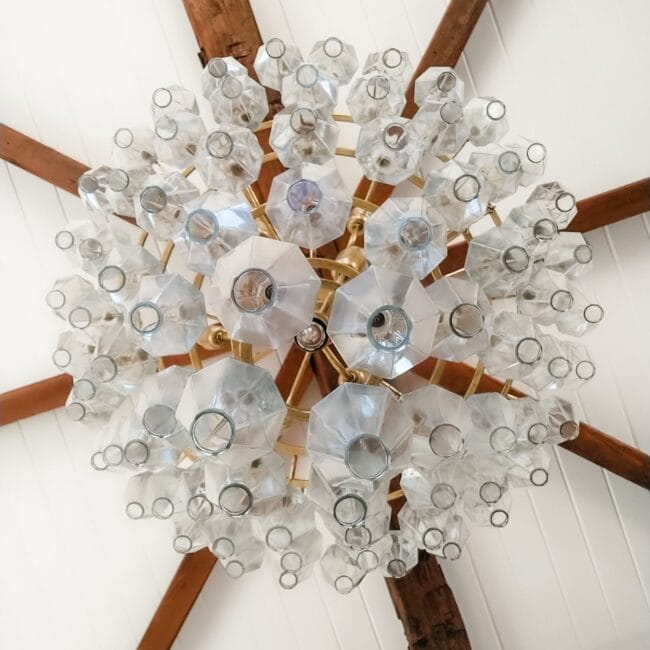 Elegant chandelier with glass shades hanging from rustic wooden ceiling beams.