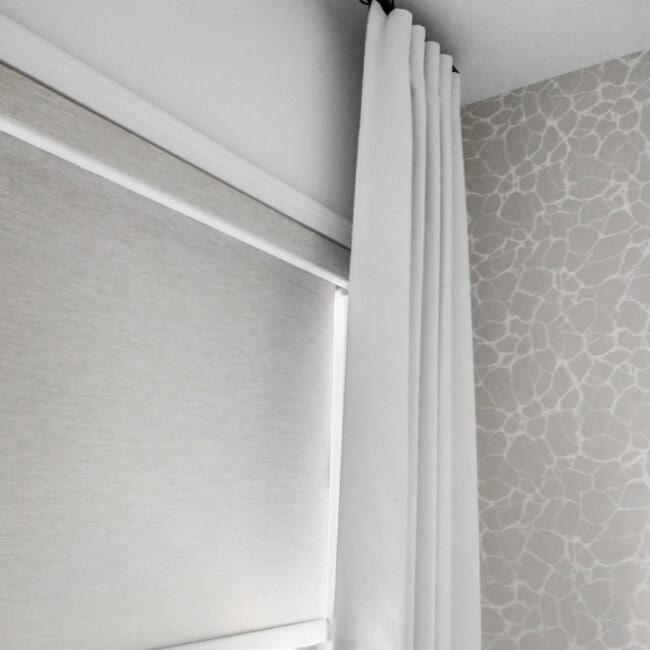 Close-up of modern white curtain paired with a beige roller blind, decorating a contemporary window.