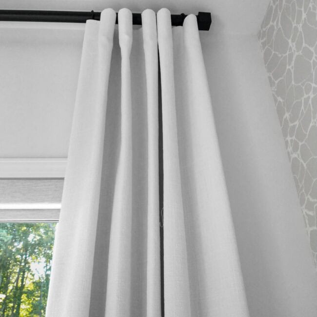 Bright white curtain in room with window view of trees outside.