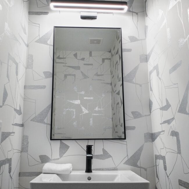 High-quality image of a contemporary bathroom featuring geometric wallpaper, a wall mirror, black faucet, and modern LED lighting.