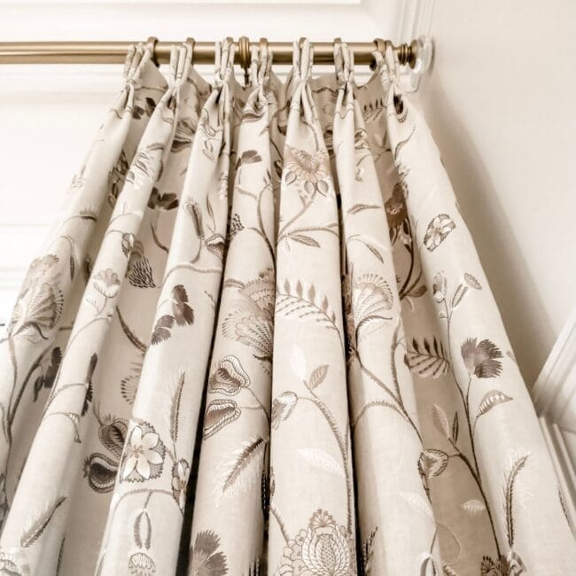 Elegant floral patterned curtain with beige tones, hanging from a polished rod in a stylish interior.