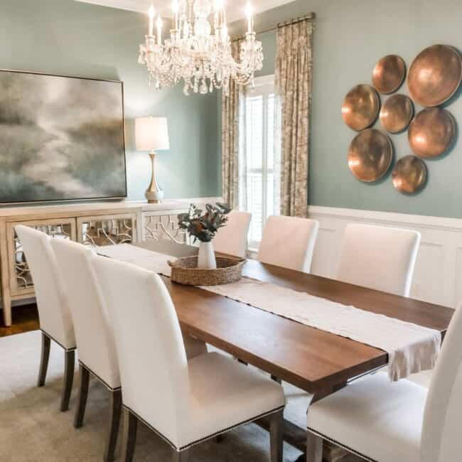 Chic dining room with a crystal chandelier, white upholstered chairs, and soothing wall colors.