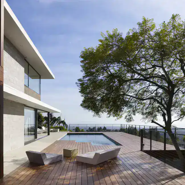 Modern house exterior with a pool and wooden deck, featuring clean lines, large glass windows, and minimalist furniture.
