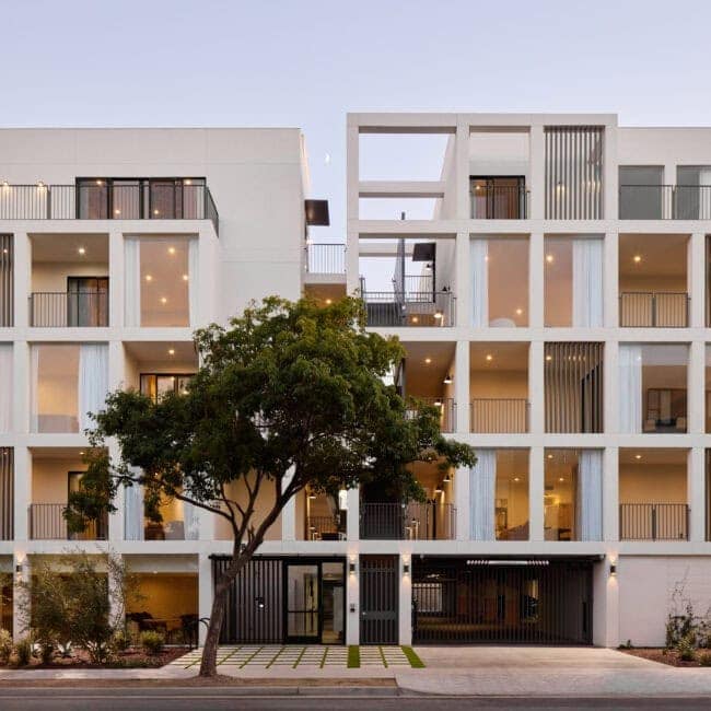 Contemporary white residential building with open balconies, vertical slatted privacy screens, and large glass sliding doors.