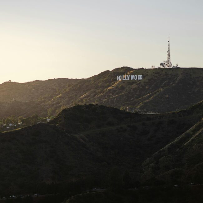 Hollywood sign on a hilly terrain with a communications tower above it, set against a clear sky at sunset.