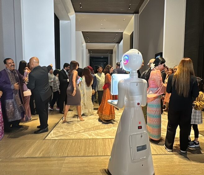 White robot photo booth moving through a busy wedding reception hall