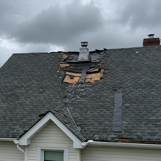 Storm-damaged roof in Rhode Island with missing shingles and visible water damage