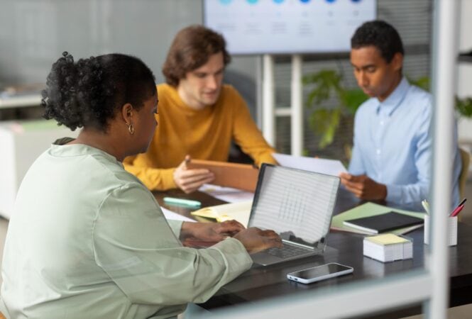 A group of people sitting around a table with laptops.