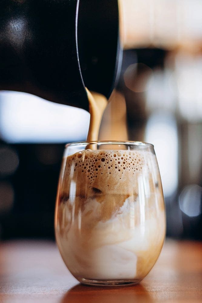 glass of coffee with cream and maple cold foam being poured