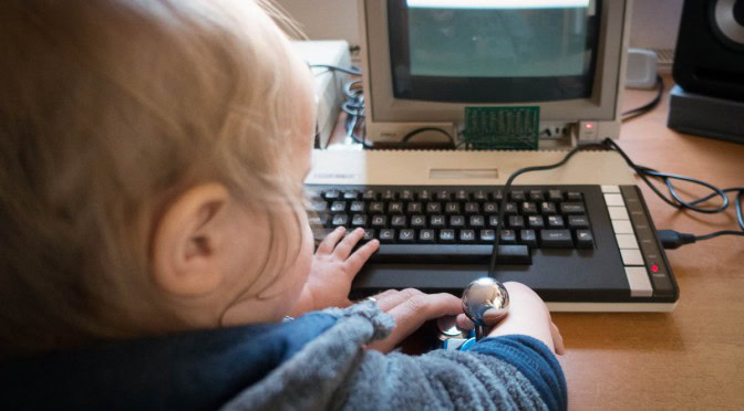 Kleinkind sitzt an einem alten 8-Bit-Computer und drückt einen Joystick-Knopf