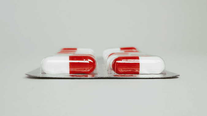 Red and white medicine capsules scattered on a white surface.