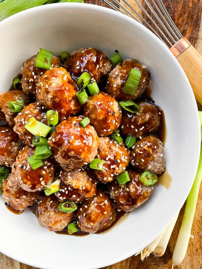 Overhead shot of asian metballs with whisk and gold fork
