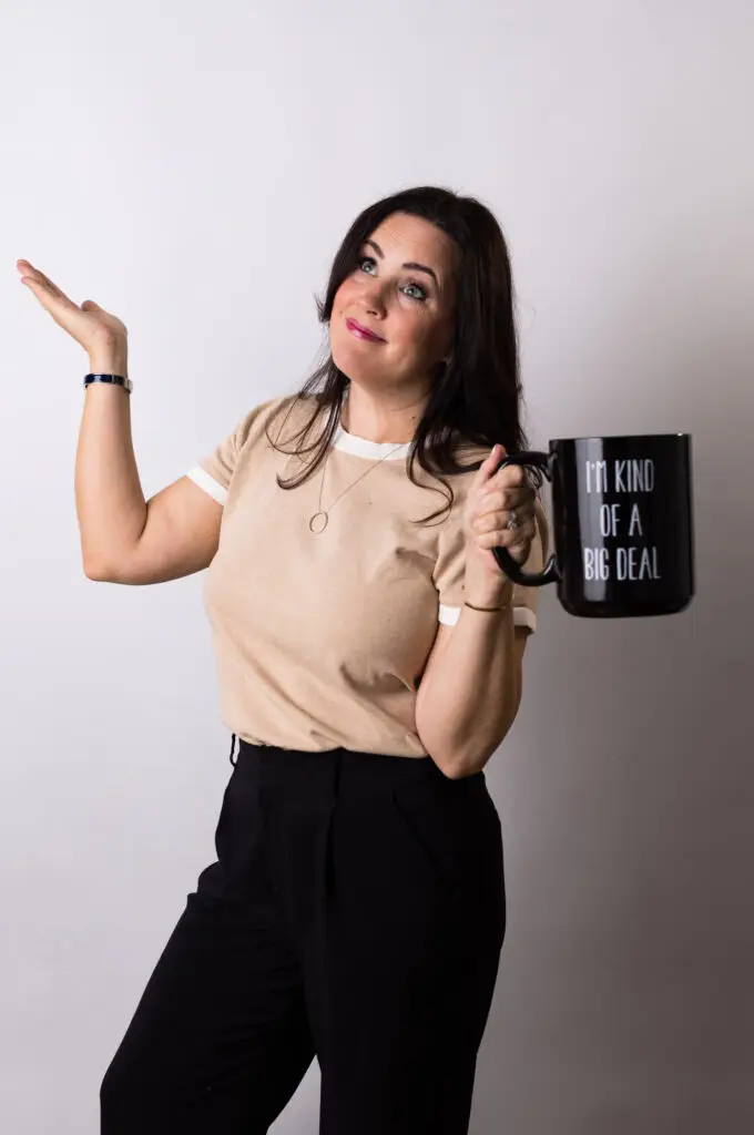 013A2741 - Jaydee Sheppard Real Estate Smiling real estate agent, Jaydee Sheppard, playfully shrugging while holding an oversized coffee mug that reads “It kind of is a big deal.