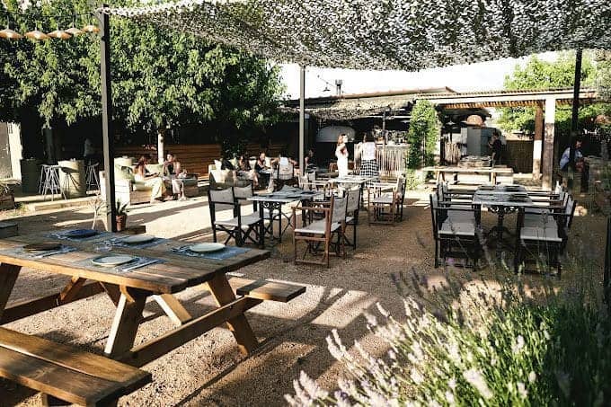 Outdoor dining area at Can Camades with stylish tables and chairs under a shaded canopy, surrounded by greenery, offering a relaxed atmosphere for guests.