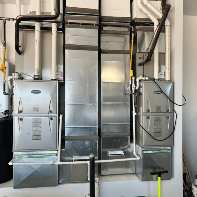Dual HVAC furnace units with ductwork and PVC piping in a utility room.