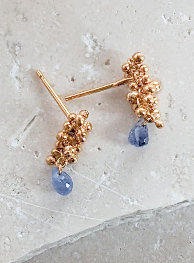 Sapphire teardop stud earrings in gold vermeil on a stone background.