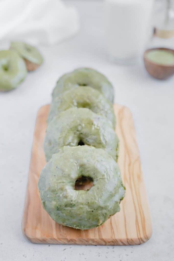 Matcha glazed donuts laying on top of a wood serving platter.