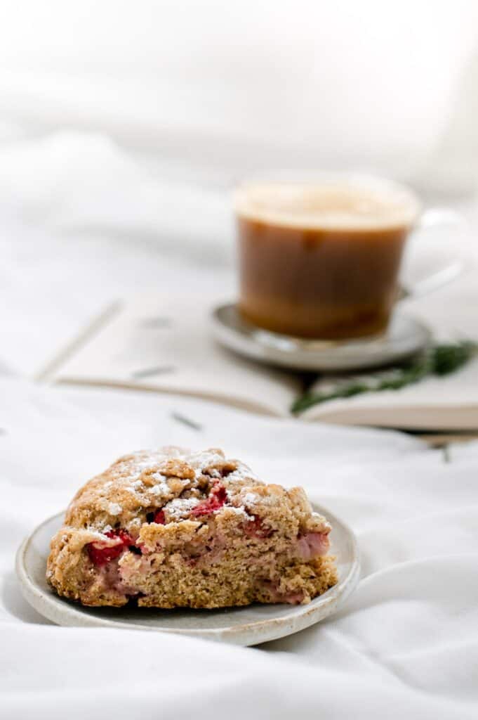 Close-up side view of vegan strawberry rosemary scones with a cup of coffee on a book in the background.
