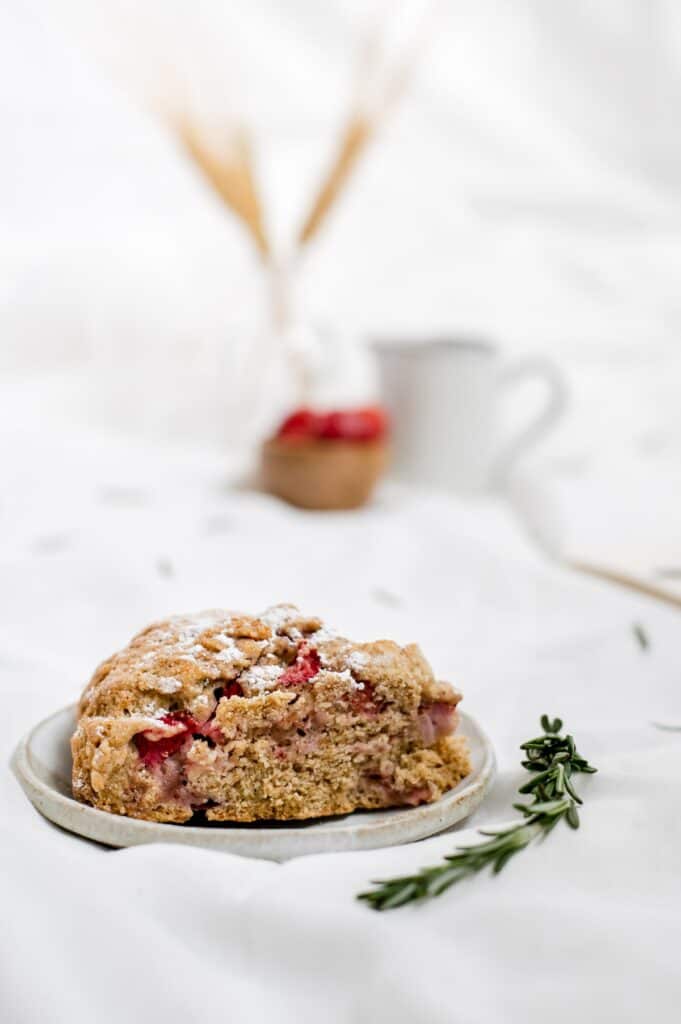 Close-up side view of vegan strawberry rosemary scones with strawberries in the background.