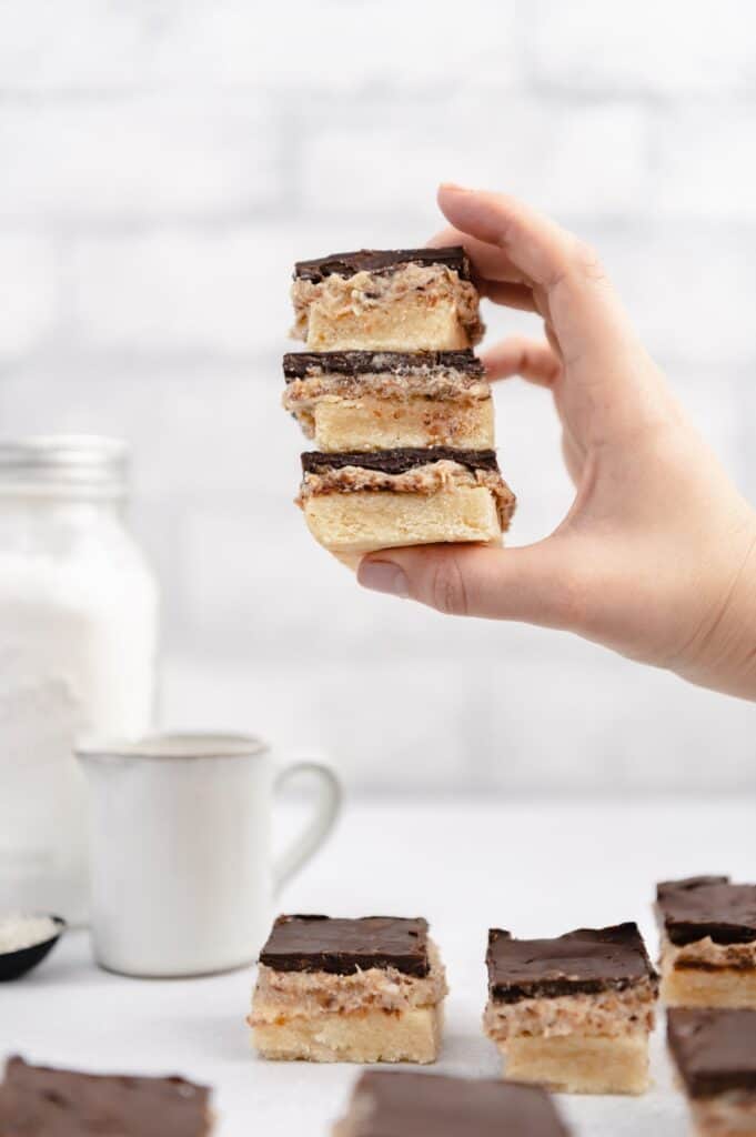 A hand holding three stacked vegan millionaire shortbread cookies with more scattered below.