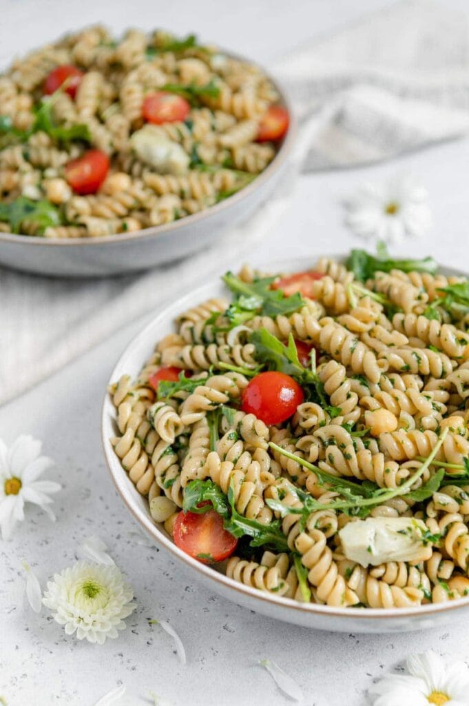 Upclose of a pesto pasta salad with tomatoes, arugula, and marinated artichoke hearts.