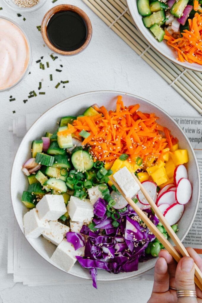 A hand holding chopsticks with a piece of sliced tofu.