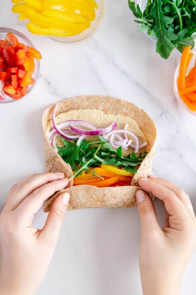 A colorful rainbow vegetable wrap being rolled.