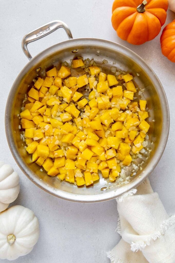 Pumpkin cubes and onions sautéing in a pan.